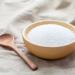 White sugar in a wooden bowl with a wooden spoon on a beige fabric