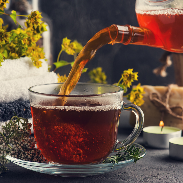 Roman provence rooibos tea in a clear teacup surrounded by herbs and candles