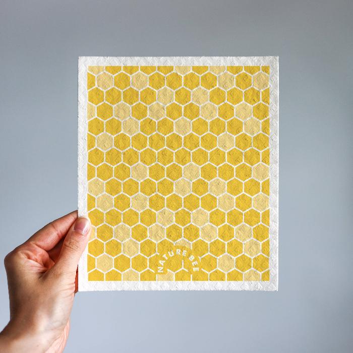 a yellow bee hive pattern dish cloth is held by a hand.