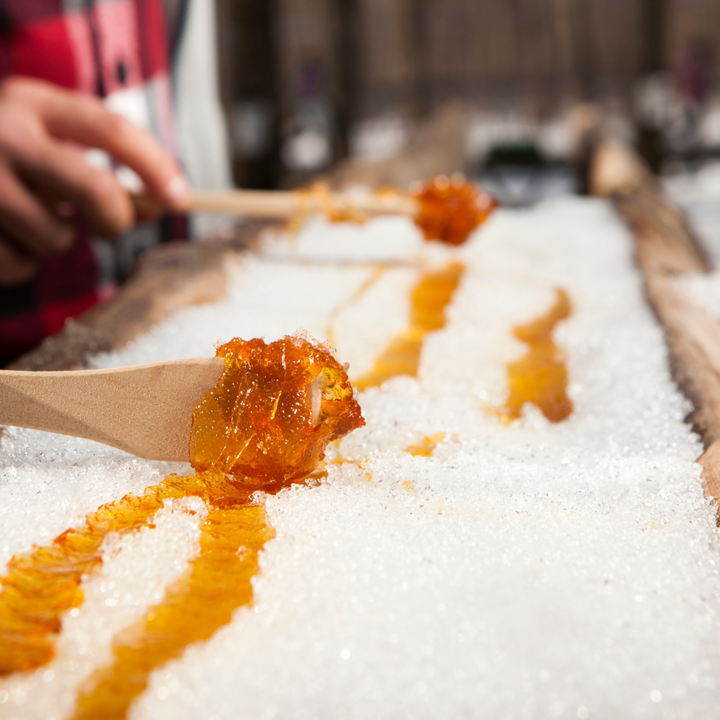 Maple taffy being prepared on top of snow using maple syrup and wooden spoons