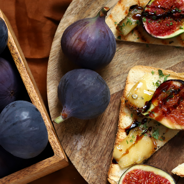 Figs on a wooden cutting board next to fig and brie toast with balsamic vinegar