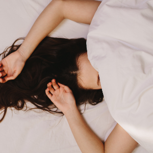 A woman sleeps with her face under soft white covers.