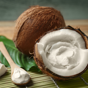 A coconut is cracked in half and filled with whipped coconut cream.  A bamboo spoon sits beside it filled with the whipped coconut.