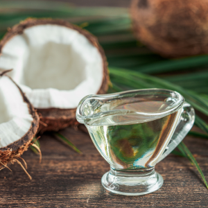 fractionated coconut oil in a glass container next to coconuts on a wooden surface