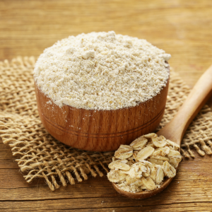 Oat flour in a wooden bowl next to a wooden spoon filled with rolled oats