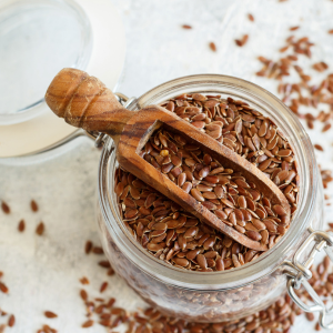 Brown flax seeds in a mason jar with a wooden scoop and a white background