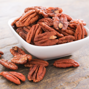 A white bowl filled with pecan halves on a wooden background