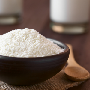 Skim milk powder in a dark wooden bowl next to a wooden spoon