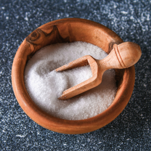 A wooden bowl filled with table salt with a wooden scoop and a blue background