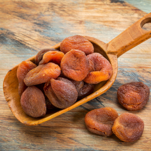 Turkish apricots in a wooden scoop with a wooden background