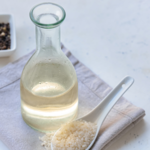 Rice vinegar in a glass bottle next to a white spoon filled with rice