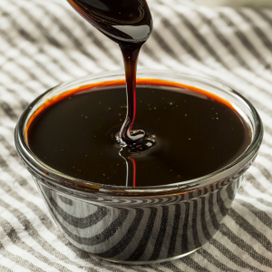 Molasses in a glass bowl on top of a cloth background with a metal spoon drizzling molasses into the bowl