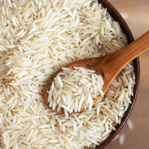 White basmati rice in a wooden bowl with a wooden spoon on a blurred wooden background