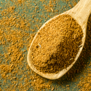 Ground cumin in a wooden spoon on a green background