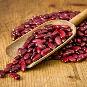 A wooden scoop filled with dark red dried kidney beans surrounded by a wooden background