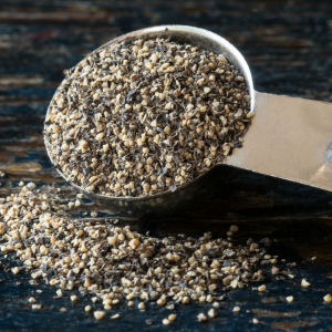 Ground black pepper in a metal spoon on top of a dark wooden background