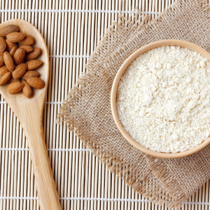 A bowl of almond flour next to a wooden spoon of almonds