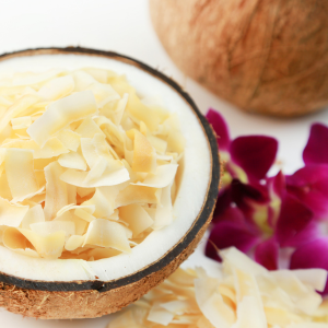 Coconut chips inside half of a coconut next to magenta flowers and another coconut