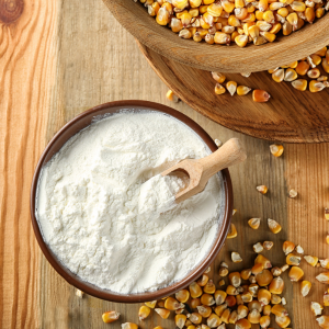 A bowl filled with cornstarch with a wooden scoop next to a bowl of dried corn kernels on a wooden background