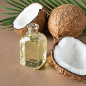 Fractionated coconut oil in a glass bottle next to coconuts on a beige background