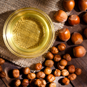 Hazelnut oil in a glass jar next to a variety of hazelnuts with a wooden background