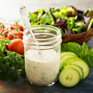 A mason jar filled with ranch dressing surrounded by a variety of vegetables