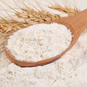 A wooden spoon filled with rye flour next to rye grain