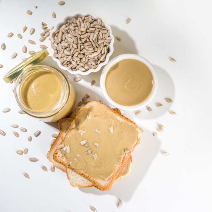 Sunflower butter in a glass jar next to sunflower seeds and toast on a white background