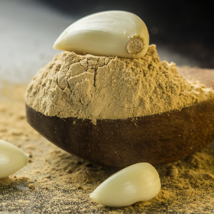 Garlic powder on a wooden spoon with some whole fresh garlic cloves