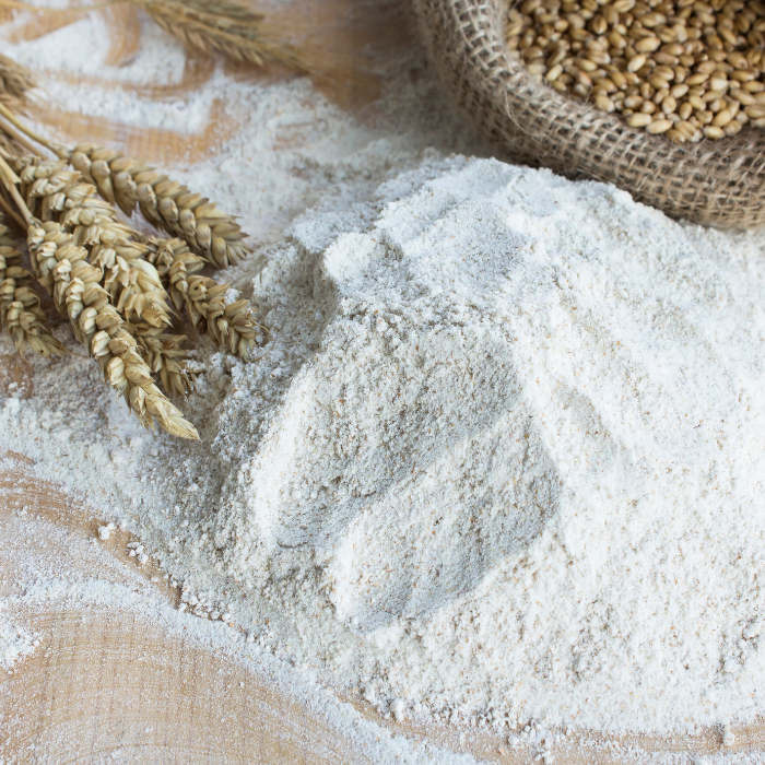 Whole wheat flour on a wooden board next to wheat plant and seeds