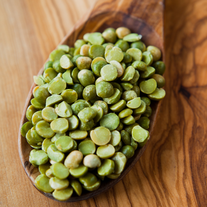 Green split peas on a wooden spoon with a wooden background