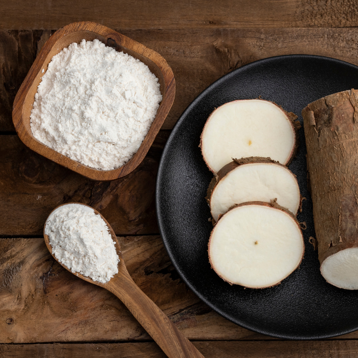 Tapioca starch in a wooden spoon and bowl next to a plate of cassava