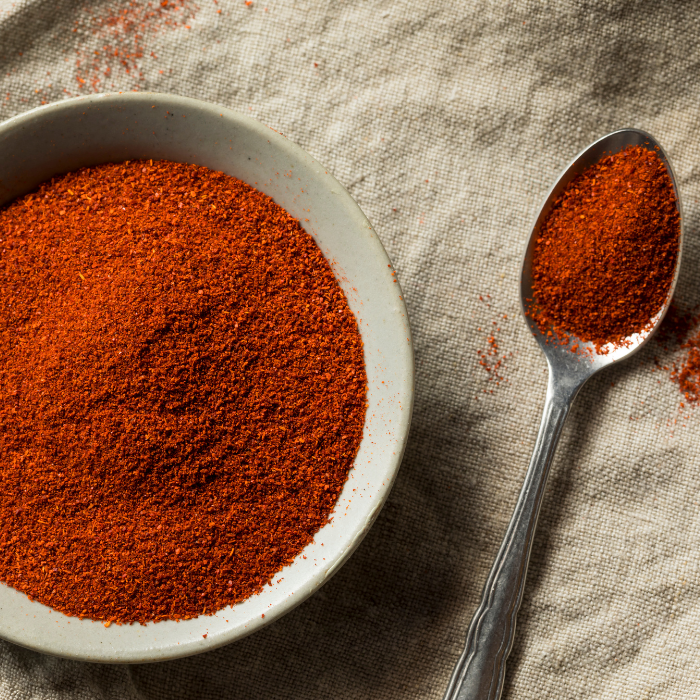 Smoked paprika in a ceramic bowl and metal spoon on a linen background