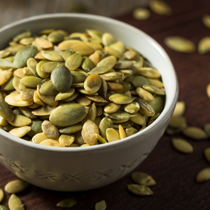 Roasted pumpkin seeds in a white ceramic bowl on a wooden surface