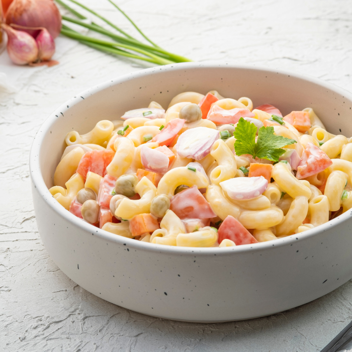 Macaroni salad in a white bowl on a white counter with shallots and green onion