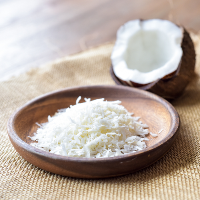 Shredded coconut in a wooden bowl on top of burlap fabric next to a coconut