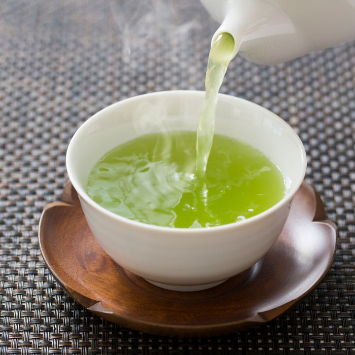 Japanese green tea being poured into a white teacup on a wooden saucer