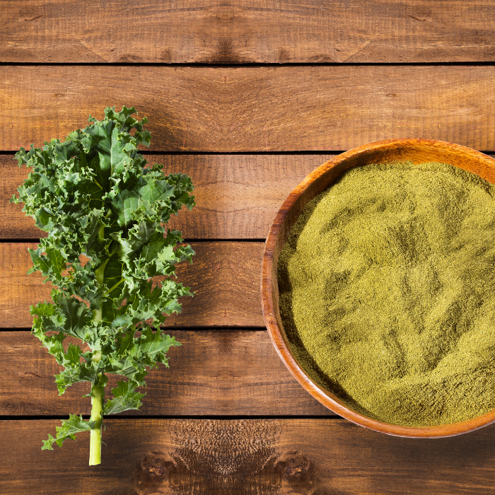 Kale powder in a wooden bowl next to kale leaves on a wooden surface