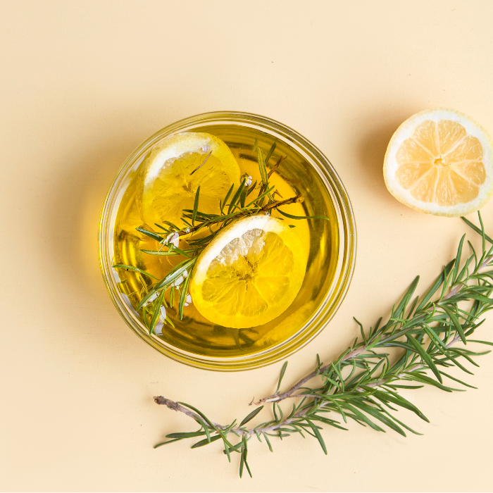 Olive oil in a clear glass jar with lemon and rosemary