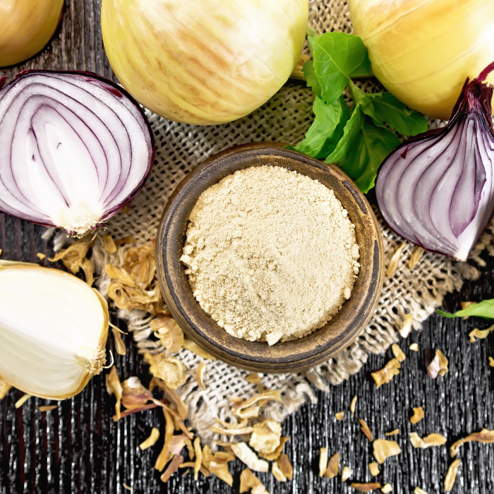 Onion powder in a wooden bowl next to a variety of onions