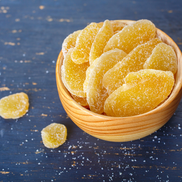 Candied ginger slices in a wooden bowl on a blue wooden surface