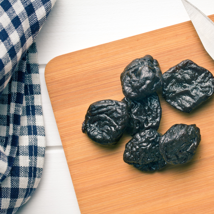 Pitted prunes on a cutting board next to a gingham towel