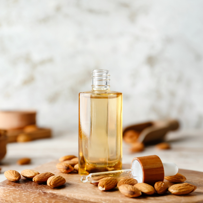 Sweet almond oil in a glass dropper bottle surrounded by almonds on a wooden surface with a white background