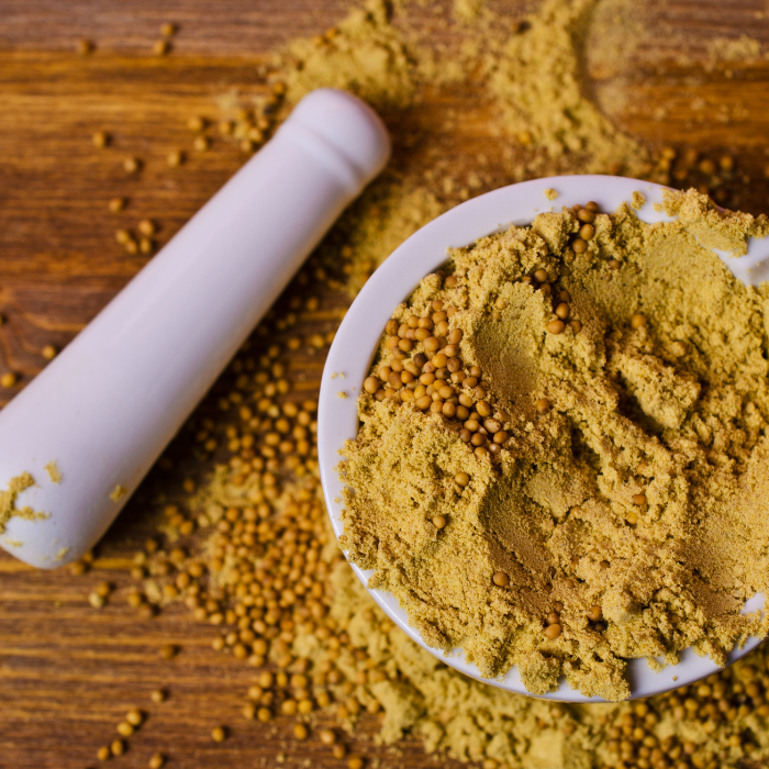 Mustard seeds and powder in a mortar and pestle on a wooden background