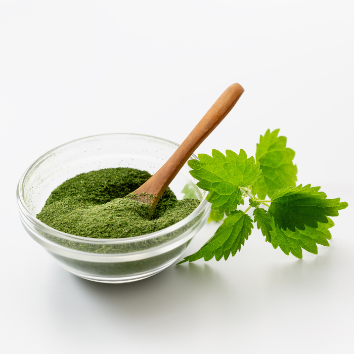 Parsley powder in a clear glass bowl next to a sprig of parsley with a white background