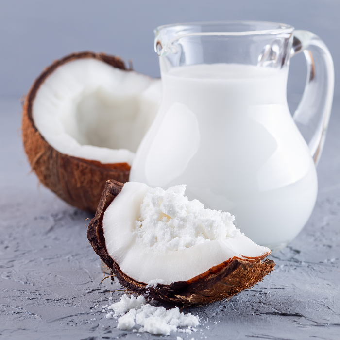 Coconut milk powder inside a coconut next to a pitcher of coconut milk on a grey/blue background