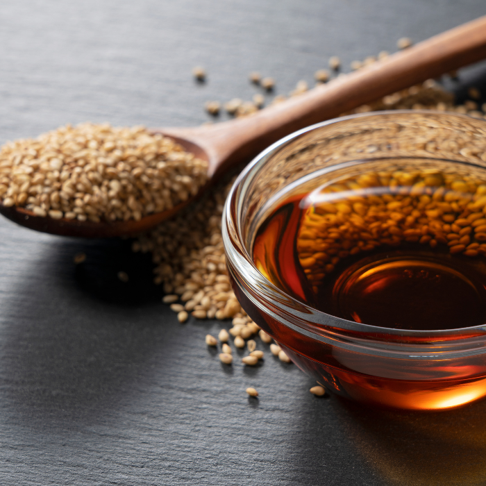 Toasted sesame oil in a small glass bowl next to a wooden spoon of sesame seeds