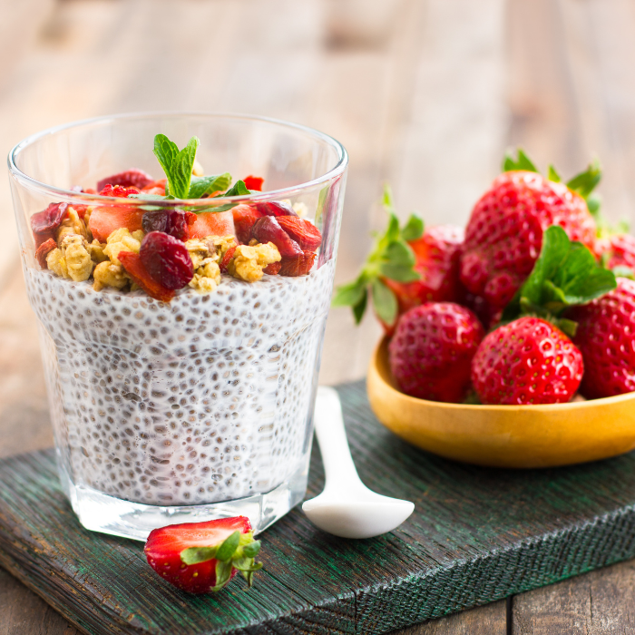 Chia pudding in a glass cup with strawberries and nuts on a wooden background