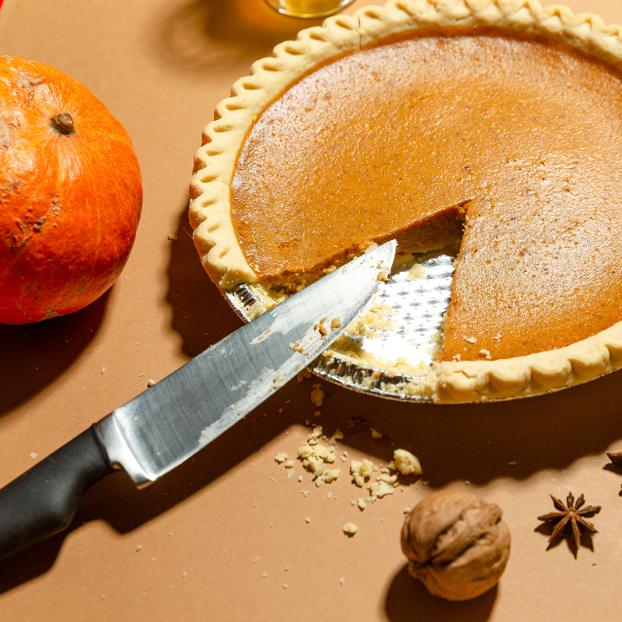 Pumpkin pie next to a pumpkin and spices on a brown surface