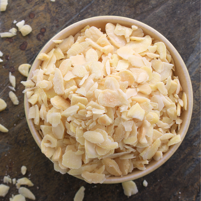 Slices almonds in a beige bowl on a dark wooden surface